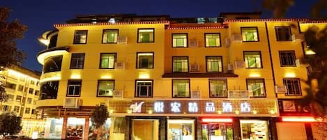 A multi-story hotel with a ground-level commercial area, featuring illuminated signage and storefronts.