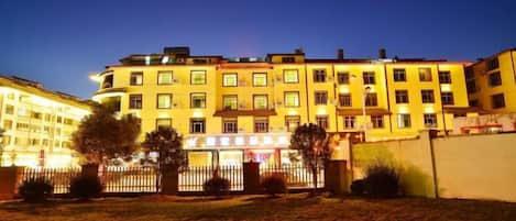 Un hotel de varios pisos con una entrada bien iluminada y un patio amurallado.