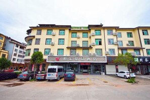 A multi-story hotel with a central entrance, parking lot, and several vehicles parked in front. - Yuehong Boutique Hotel (Wuyishan)