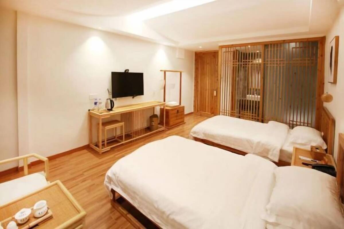 Une chambre d’hôtel avec deux lits, un bureau avec une télévision, une armoire en bois et une table de chevet avec un plateau.