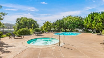 A swimming pool area with two pools, lounge chairs, and a patio.