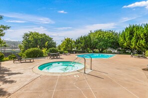 A swimming pool area with two pools, lounge chairs, and a patio.