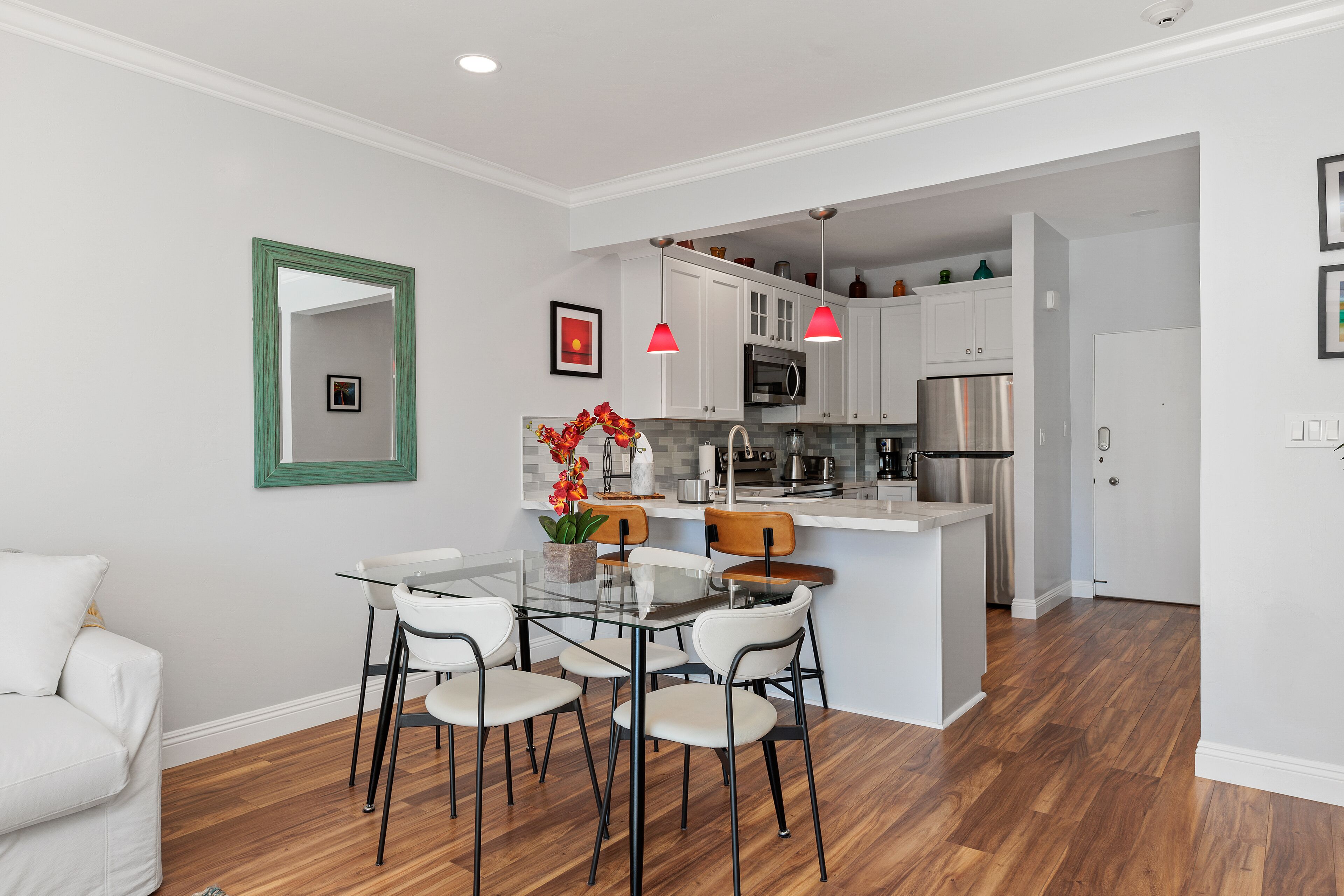 A modern kitchen with white cabinets, stainless steel appliances, and a glass dining table with chairs.