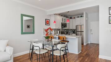 A modern kitchen with white cabinets, stainless steel appliances, and a glass dining table with chairs.