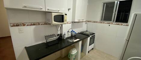 A compact kitchen with white cabinets, a microwave, a stove, and a refrigerator.
