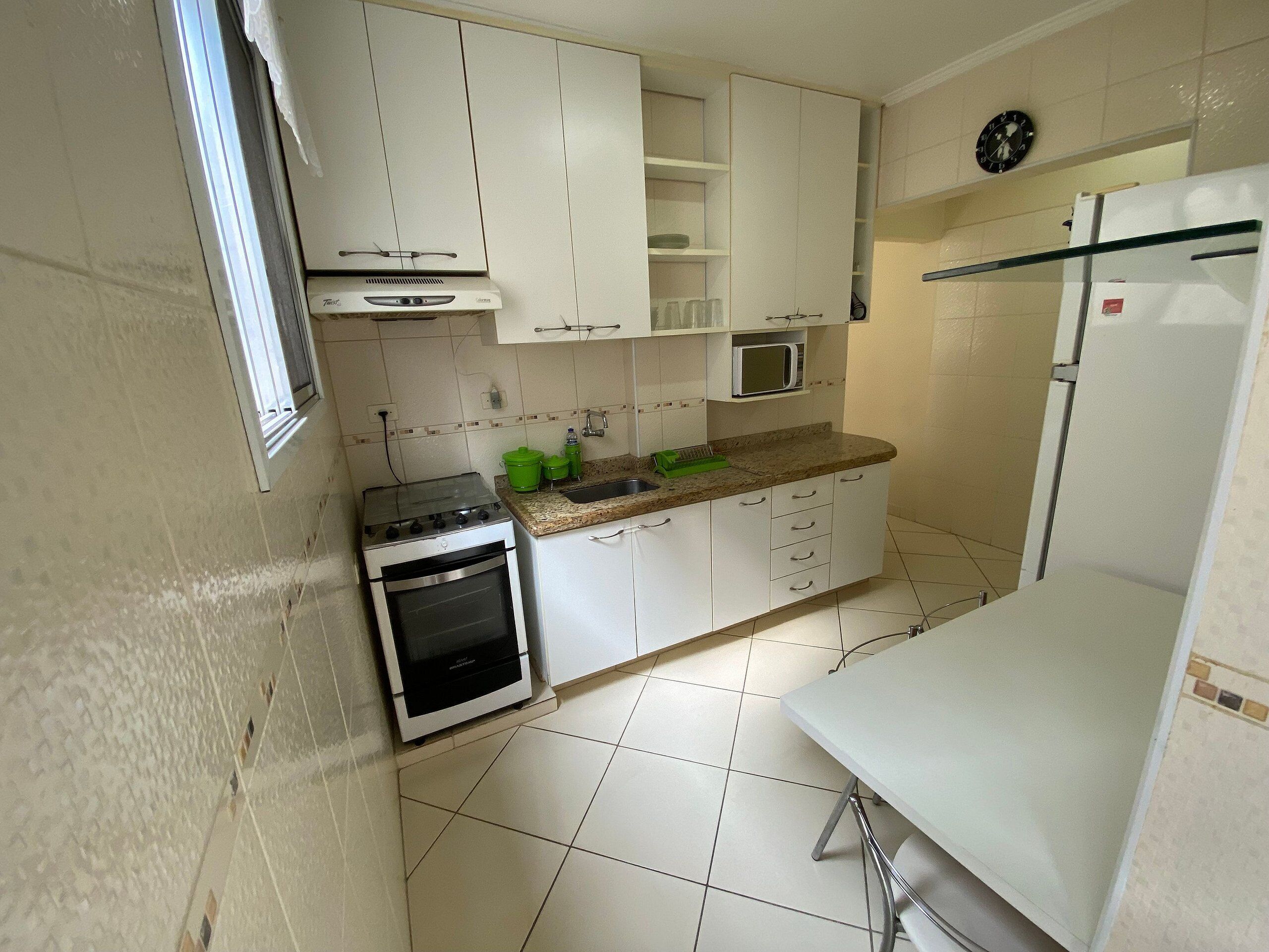 Una cocina compacta con armarios blancos, estufa, microondas y refrigerador.