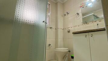 Een badkamer met een douchecabine van glas, een toilet en een wastafel met spiegel erboven.