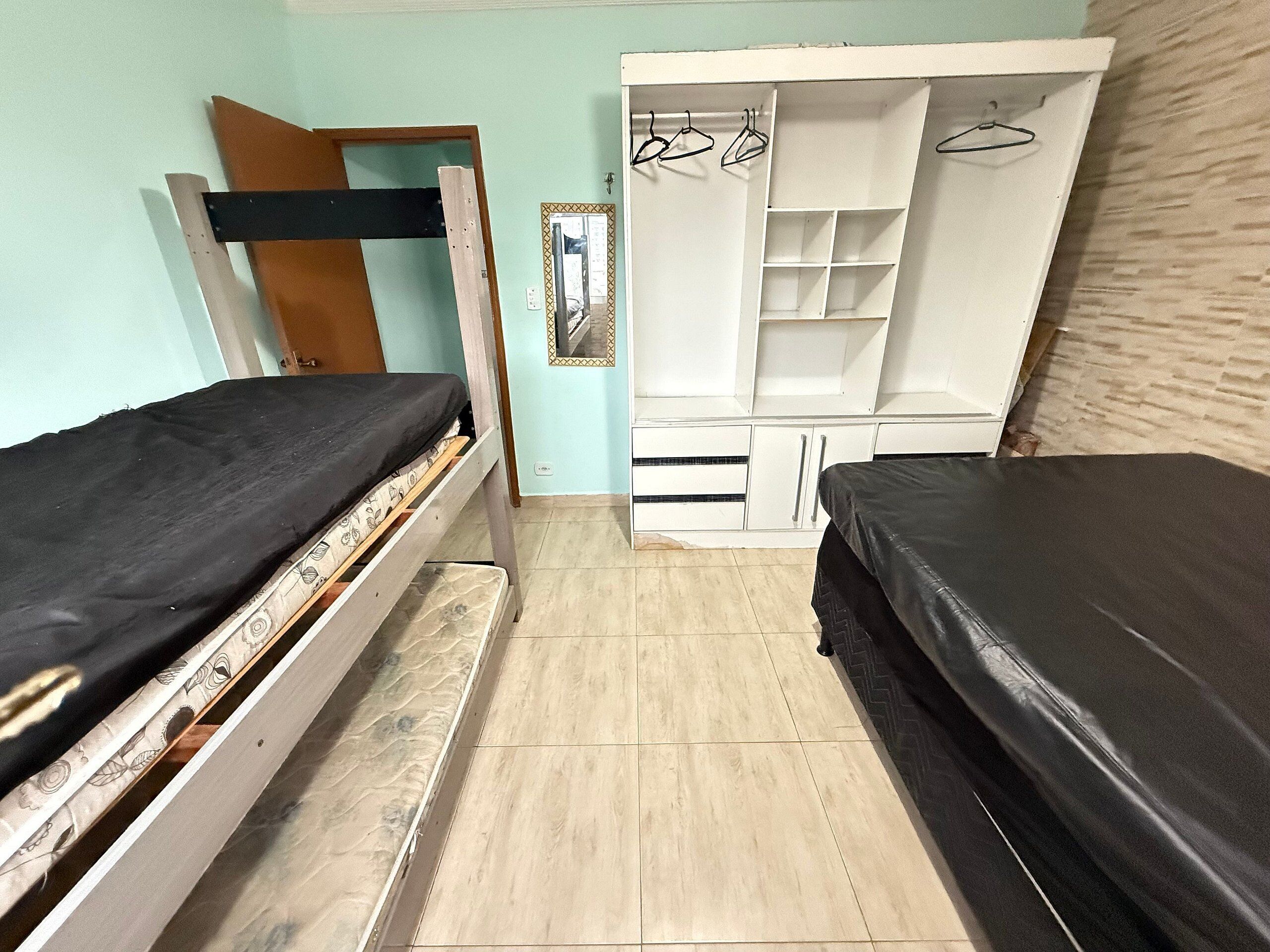 Una habitación pequeña y funcional con dos camas individuales, un armario con espacio para colgar ropa y un espejo.