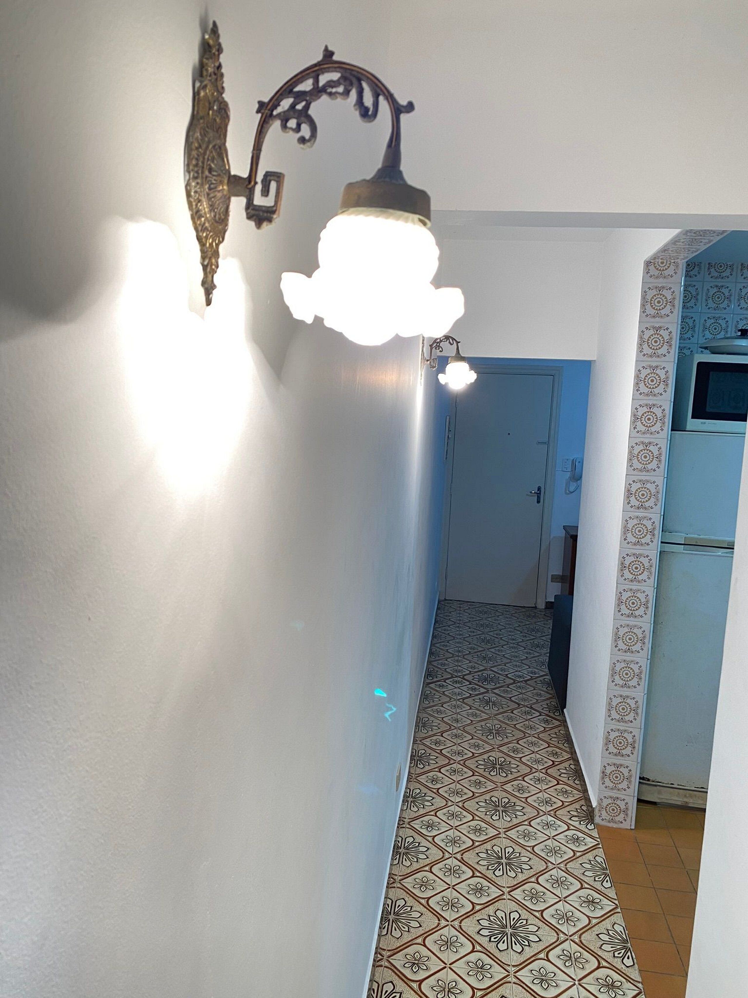 A hallway with patterned floor tiles, a light fixture, and a door leading to a kitchen area.
