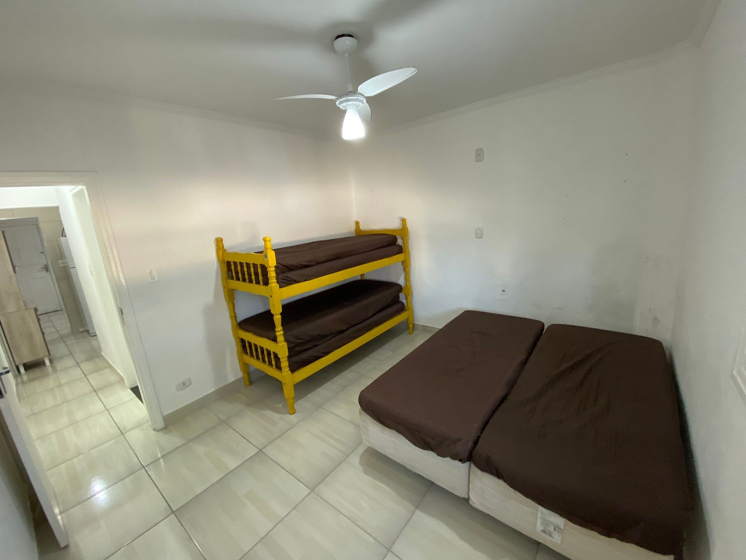 A small, clean room with a bunk bed, a single bed, and a ceiling fan.