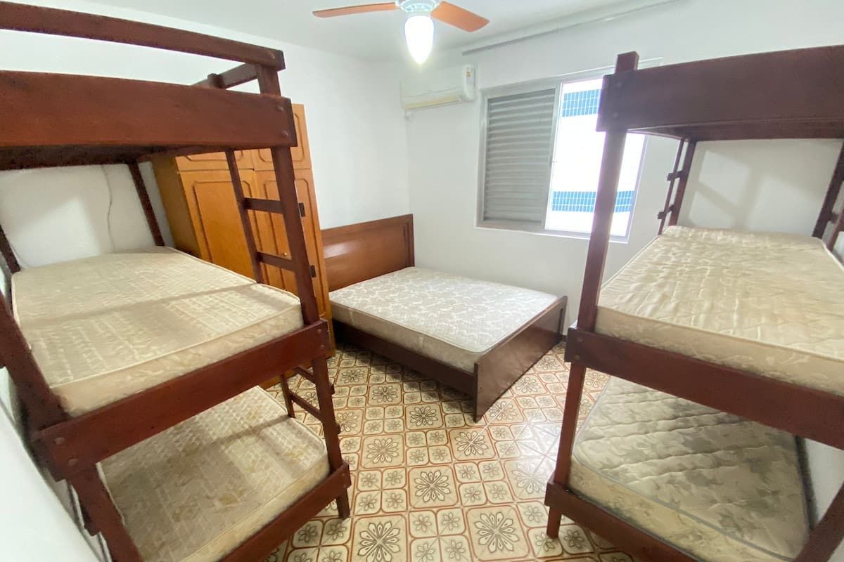 A room with three bunk beds, a small bedside table, and a window with blinds.
