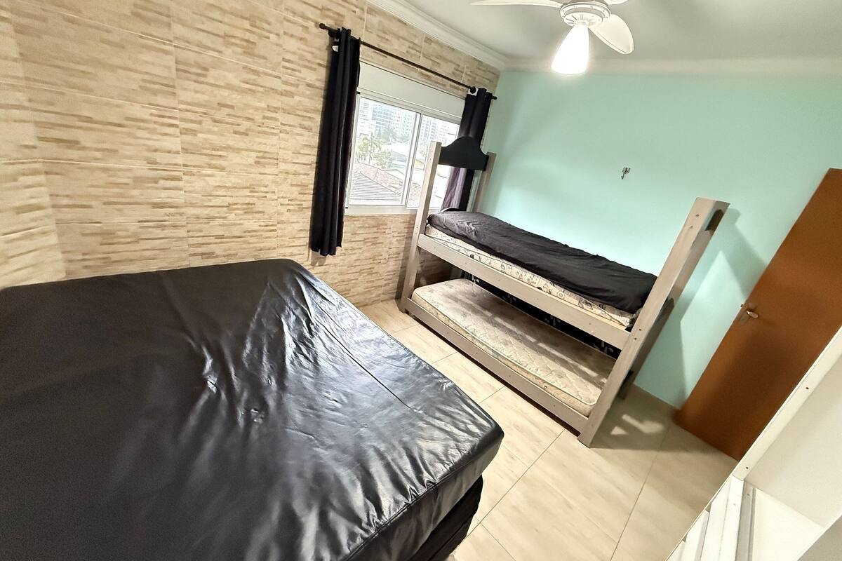 A room with a bed, a window with curtains, a ceiling fan, and a door.