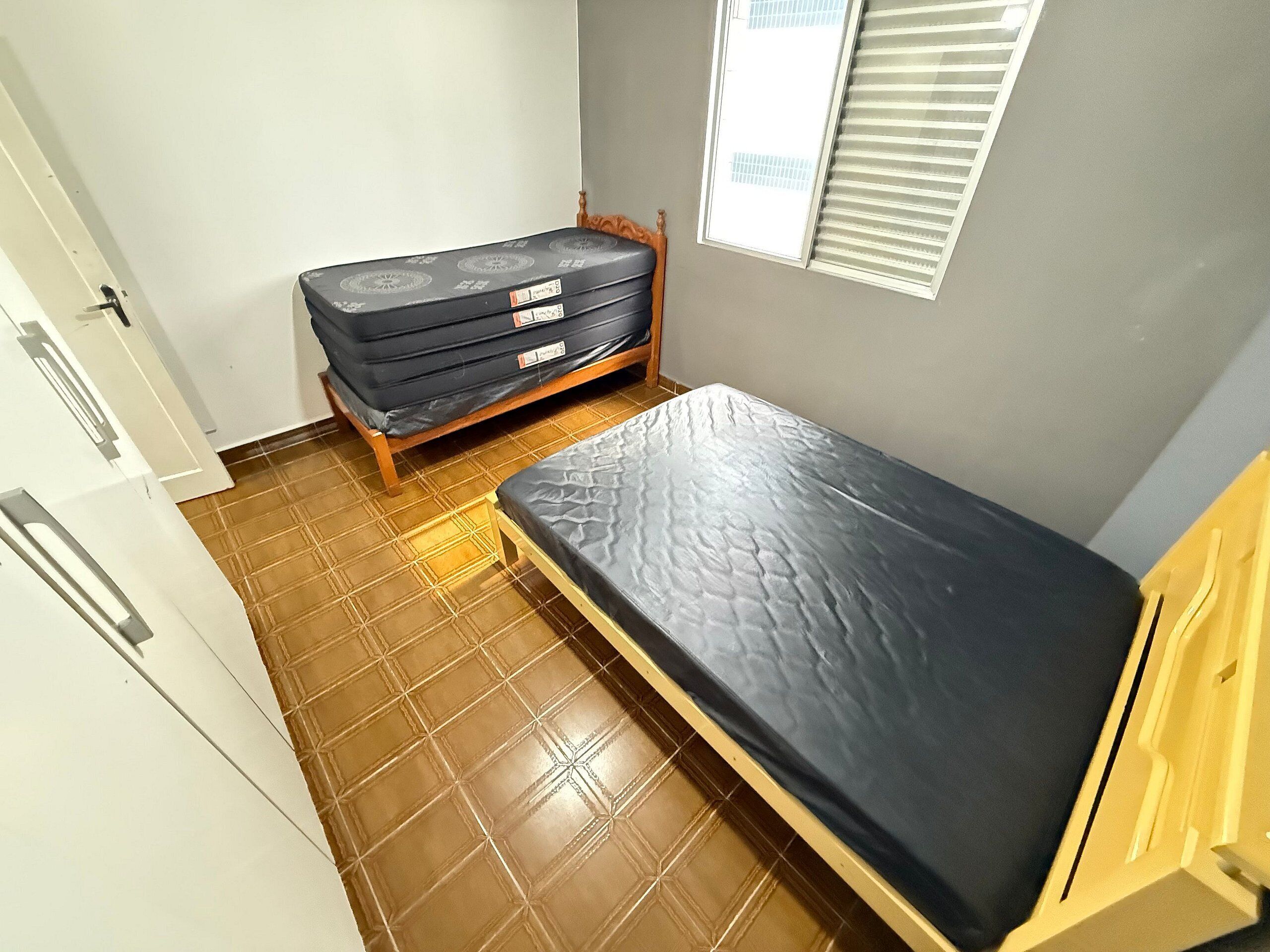 A small, compact room with a single bed, a wooden wardrobe, and a window with blinds.
