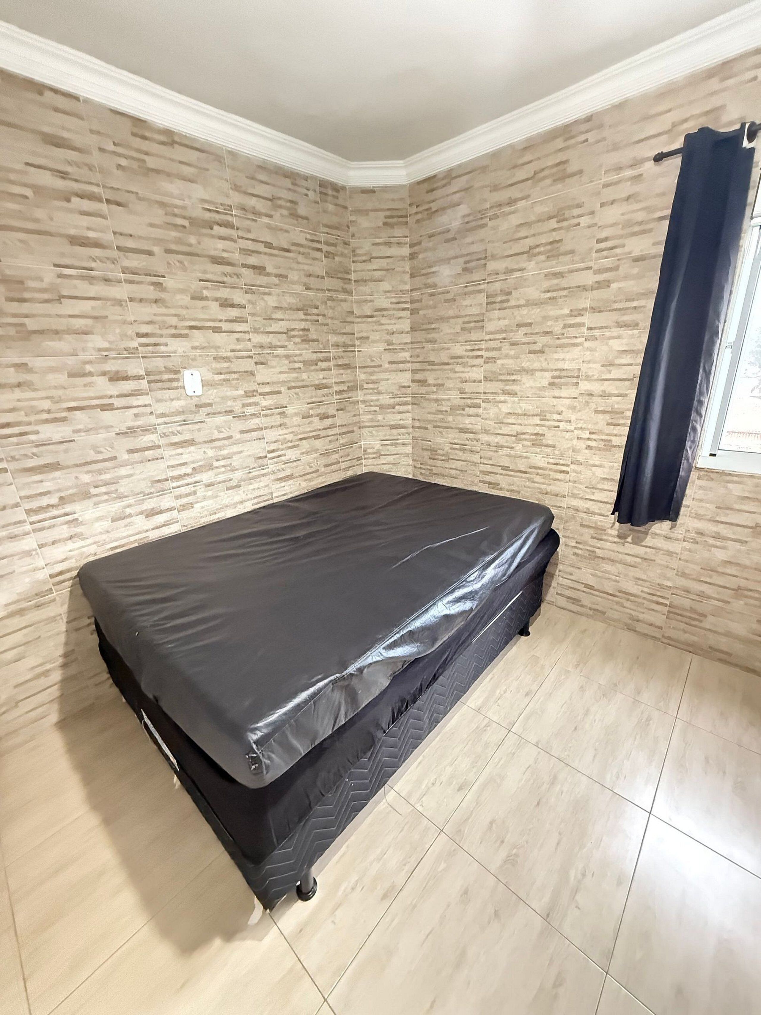A room with a bed, tiled walls, and a window with curtains.