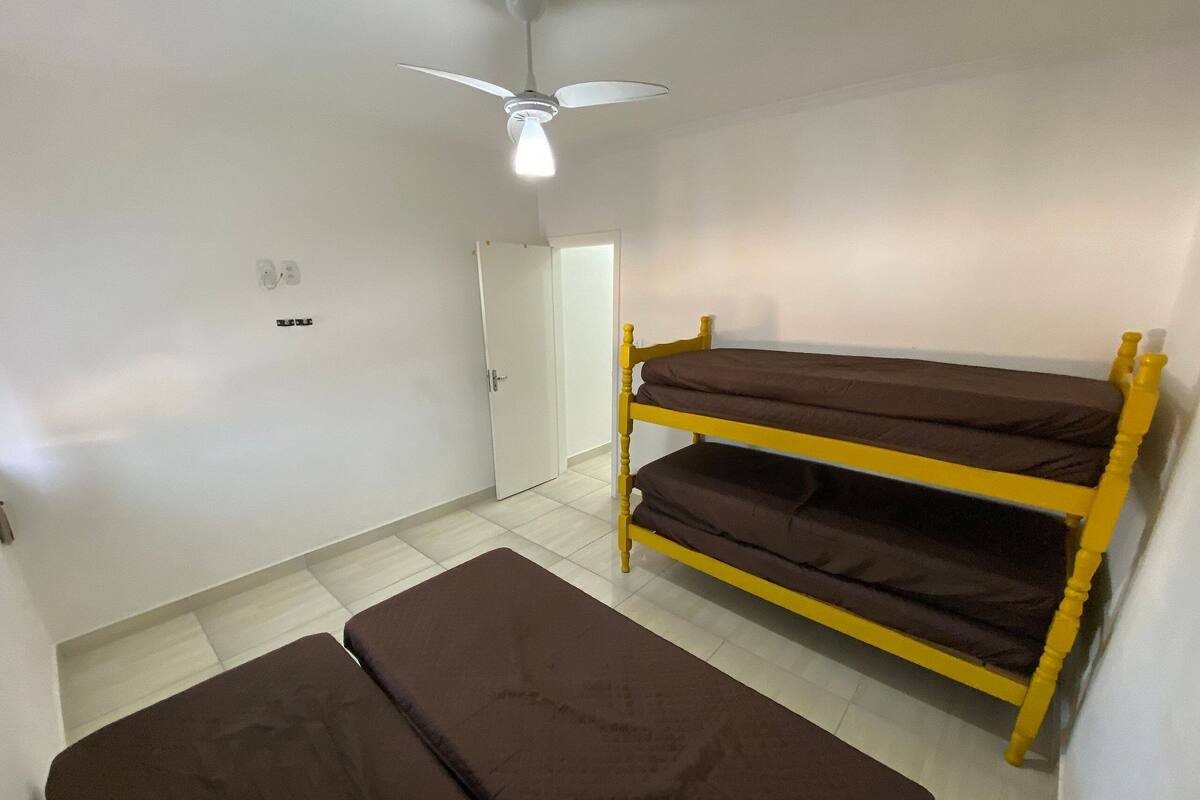 A room with a bunk bed, a single bed, a ceiling fan, and a door.