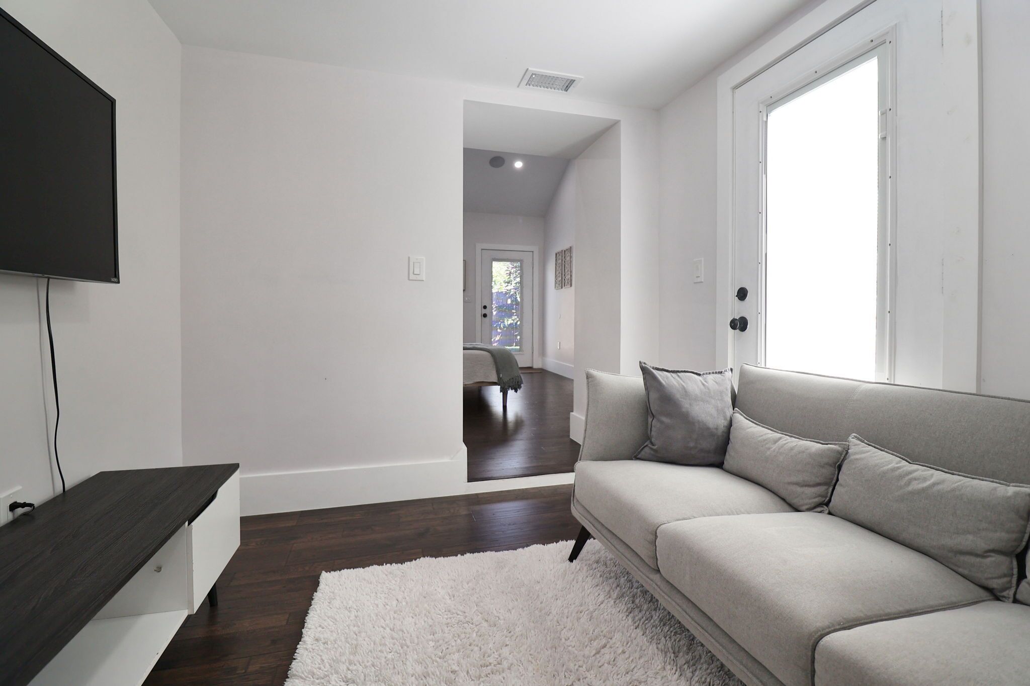 Un salon moderne avec un téléviseur à écran plat, un canapé gris, un tapis blanc et un plancher en bois.