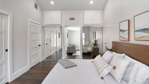A spacious bedroom with a large bed, a wooden headboard, and a view of a hallway with doors.