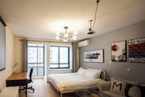 Un dormitorio moderno con una cama, un escritorio y una silla. Hay una ventana con cortinas, una lámpara de techo y una obra de arte en la pared.