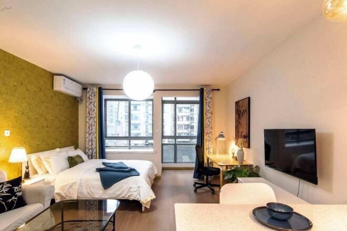 A hotel room with a bed, a desk, a TV, and a window with a city view.