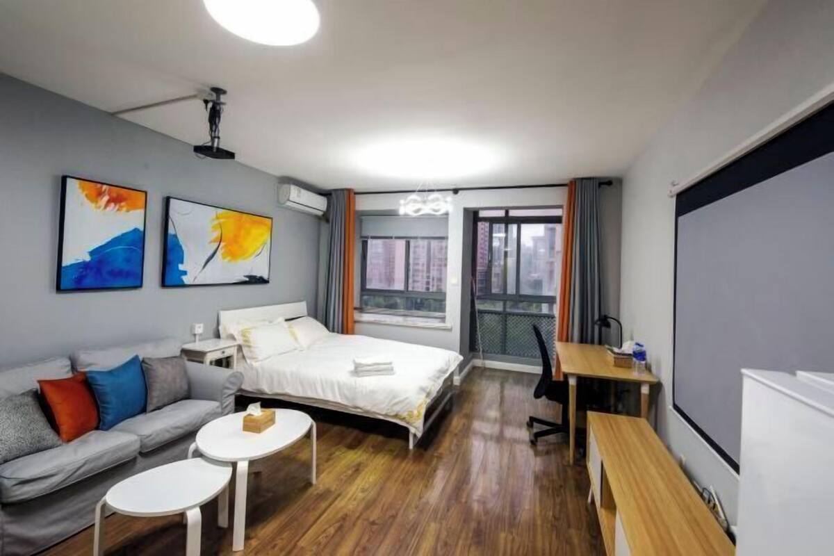 A modern hotel room with a bed, a sofa, a desk, and a large window.