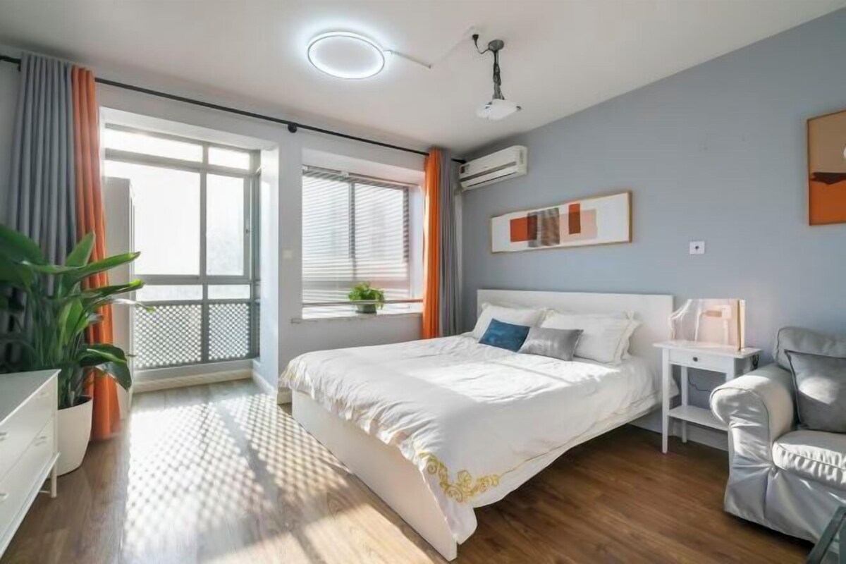 A modern bedroom with a large bed, a bedside table, a chair, and a window with curtains.