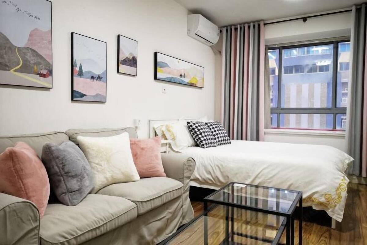 A modern hotel room with a bed, a sofa, a glass coffee table, and artwork on the walls.
