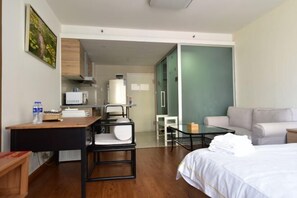 A hotel room with a bed, a desk with a chair, a small table, a sofa, and a kitchenette area.