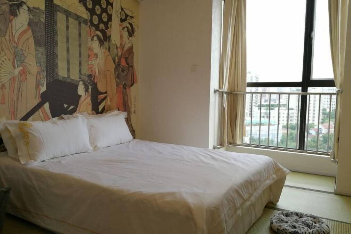 A bedroom with a large bed, a window with curtains, and a wall with a traditional Japanese painting.