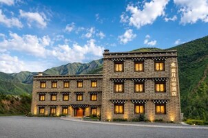 Un hotel de varios pisos con una fachada simétrica, numerosas ventanas y un paisaje montañoso de fondo.