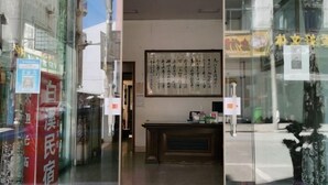 Entrada de un hotel con una obra de caligrafía japonesa tradicional en la pared, un mostrador de recepción y un letrero que indica la habitación número 25.