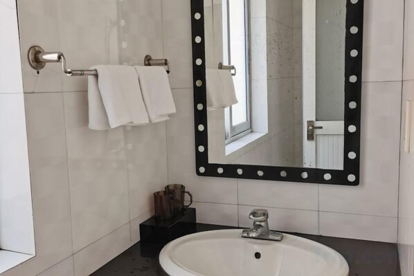 A bathroom with a sink, mirror with lights, and towels on a rack.