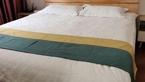 Una cama bien hecha con una colcha verde y blanca a rayas, un cabecero de madera y una mesita de noche con una lámpara.