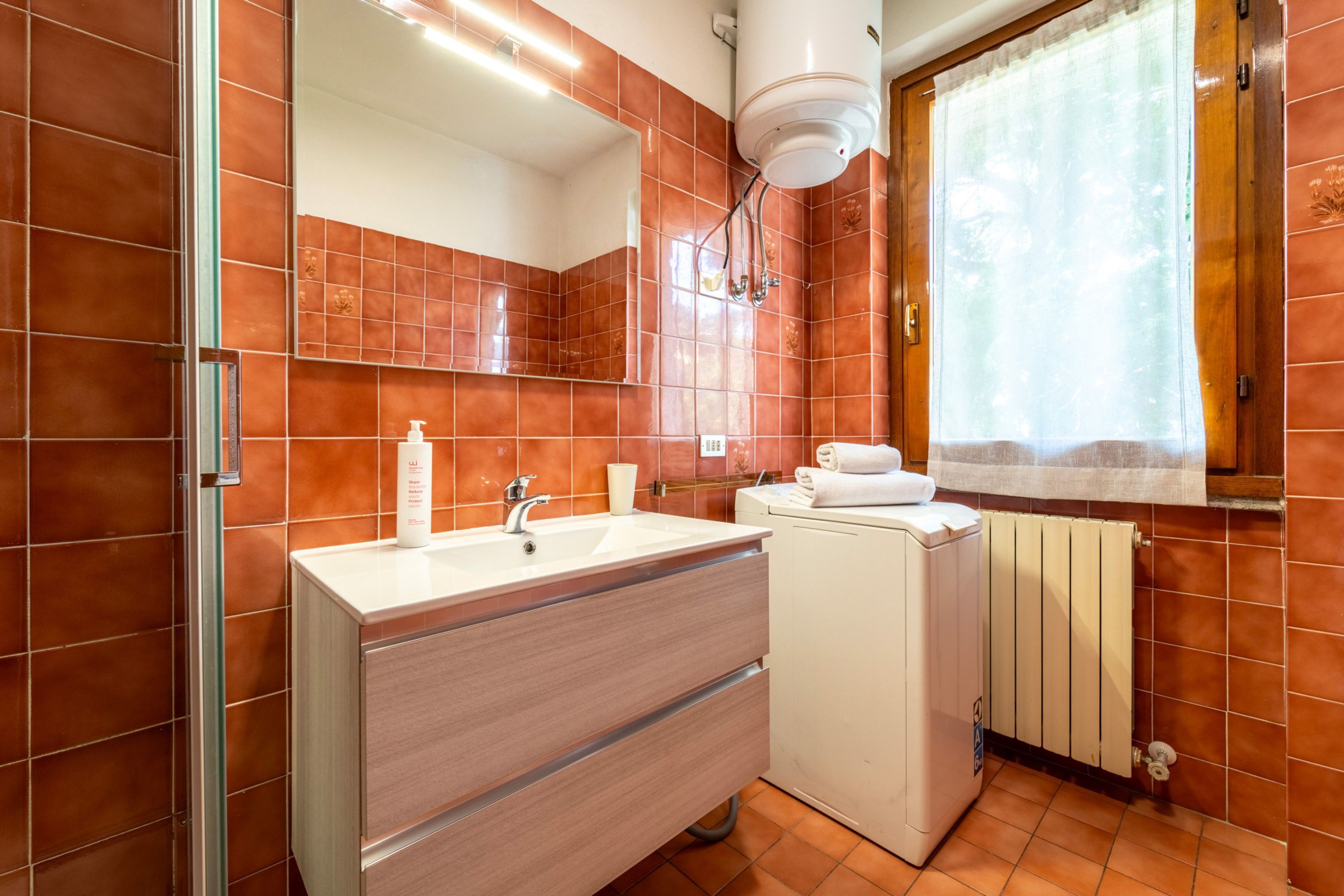 A bathroom with a white sink, mirror, and towel rack. There is a window with a curtain and a radiator.