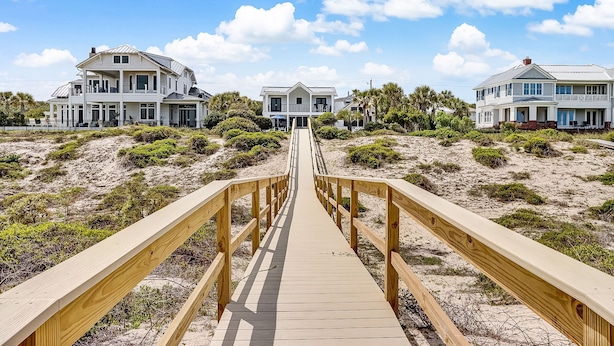 Une promenade en bois qui mène à des propriétés situées en bord de mer, avec plusieurs étages et des balcons.