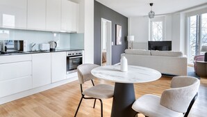 A modern kitchen with white cabinets, a dining table with chairs, and a living area with a sofa and TV. - Modern Horgen 2.5 Room w/ Storage & W/D, 3 min to Market, by Blueground (Zurich)