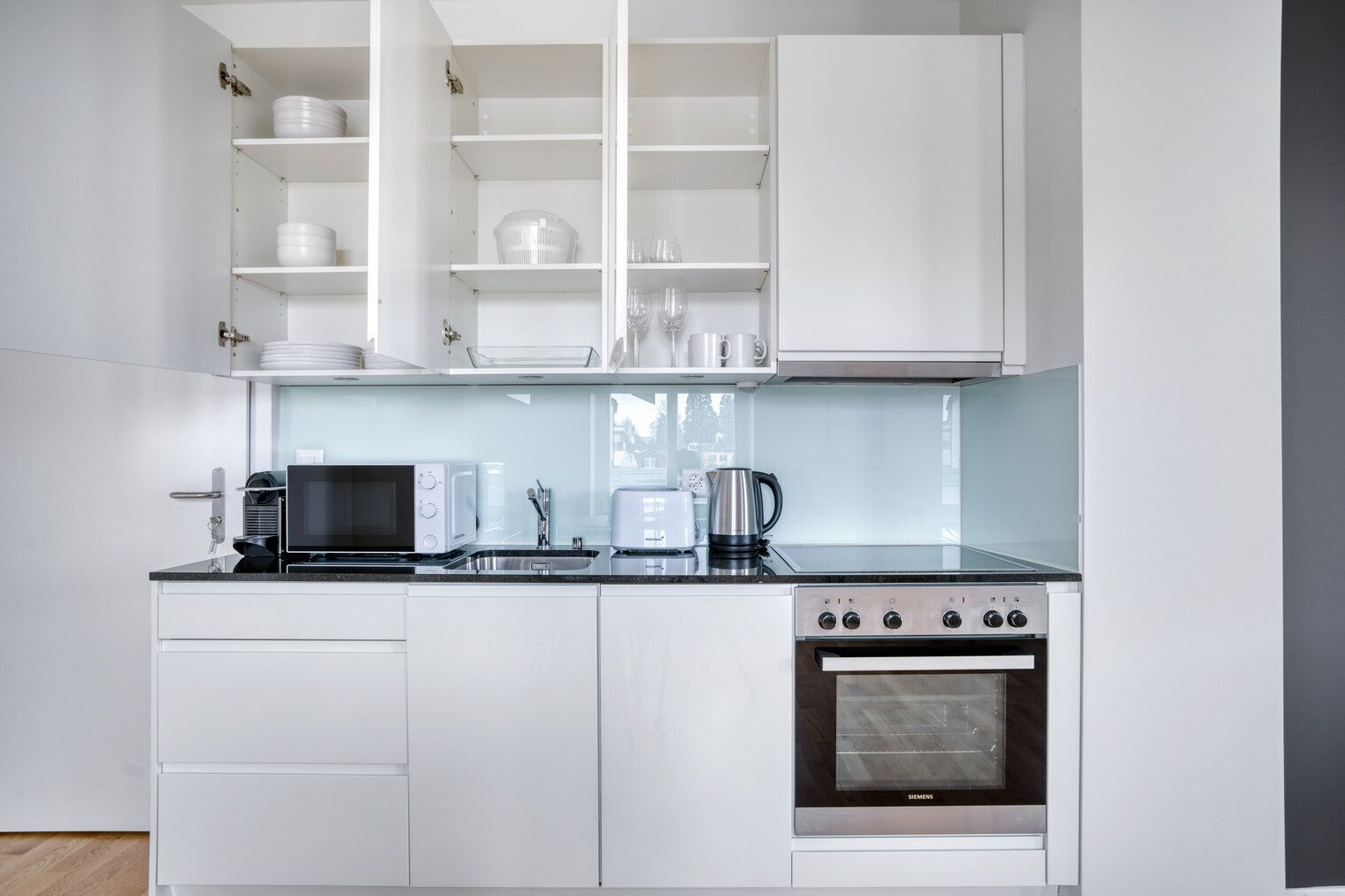 A modern kitchen with white cabinets, a stainless steel oven, a microwave, a toaster, and a kettle.