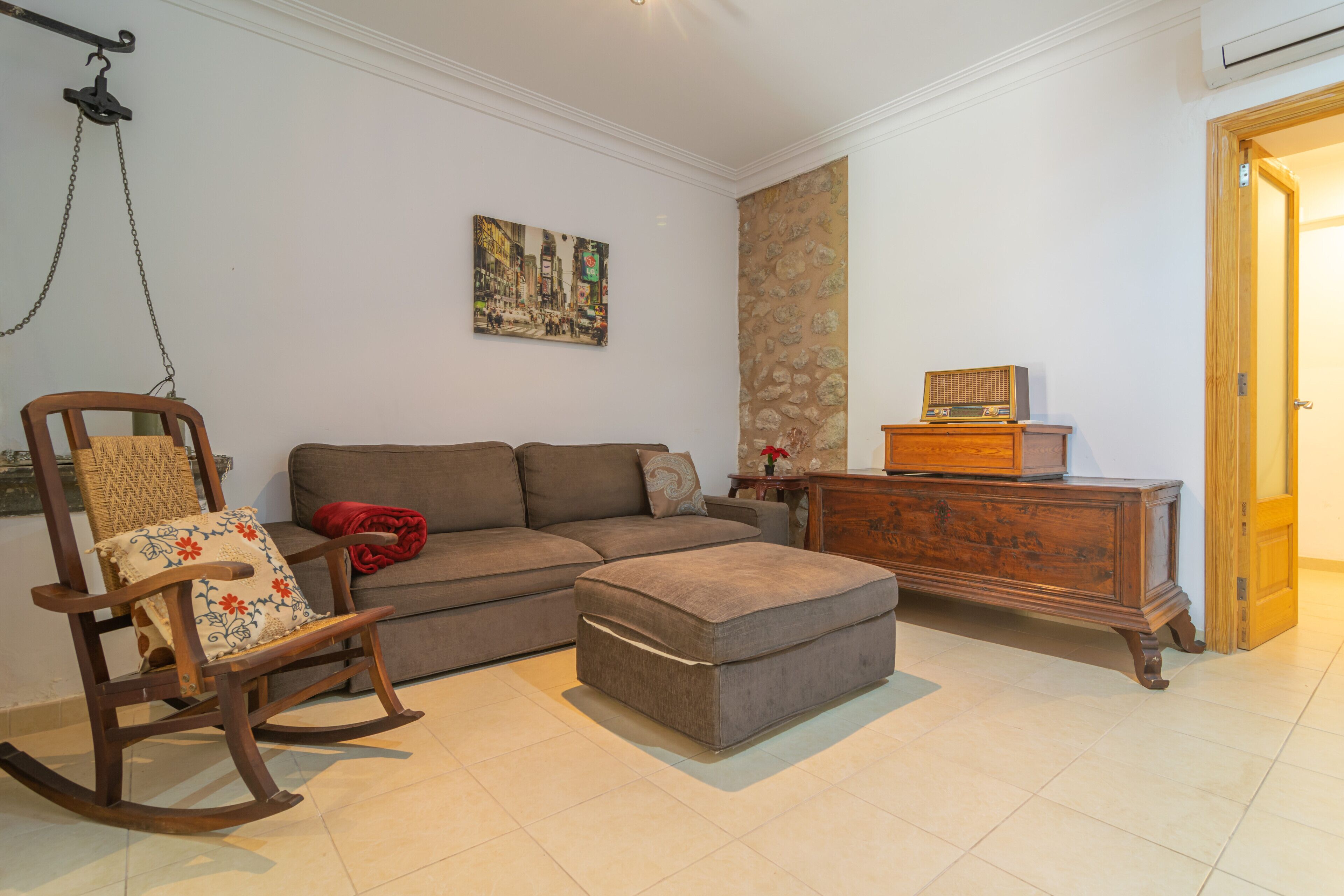Ein Wohnzimmer mit Sofa, Hocker, Schaukelstuhl und einem Holzschrank.