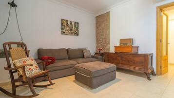 Ein Wohnzimmer mit Sofa, Hocker, Schaukelstuhl und einem Holzschrank.