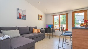 Un salon moderne avec un canapé gris, une petite table à manger et un téléviseur.