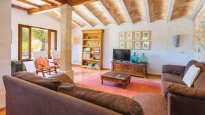 Uma sala de estar ampla com teto de madeira, estante, televisão e assentos confortáveis.