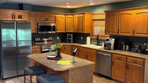 A kitchen with wooden cabinets, stainless steel appliances, a central island with stools, and a coffee station. - Newly remodeled Lake Frontage Cabin Hot Tub Arcade 2 Fire pit areas TRIPLE Decks (Golden)