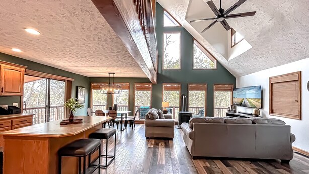 A spacious living area with a large sofa, a dining table, and a kitchen area with a bar. - Newly remodeled Lake Frontage Cabin Hot Tub Arcade 2 Fire pit areas TRIPLE Decks (Golden)