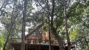 A cabin surrounded by trees, with a wooden deck and a covered porch. - Newly remodeled Lake Frontage Cabin Hot Tub Arcade 2 Fire pit areas TRIPLE Decks (Golden)
