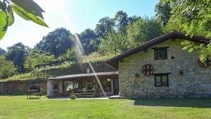 A stone building with a covered patio, surrounded by a grassy lawn and trees. - Casa Yolanda - country house in the Picos de Europa, Arenas de Cabrales (Arenas De Cabrales)
