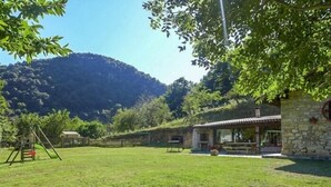 A stone building with a patio, a swing set, and a grassy yard with a mountain backdrop. - Casa Yolanda - country house in the Picos de Europa, Arenas de Cabrales (Arenas De Cabrales)