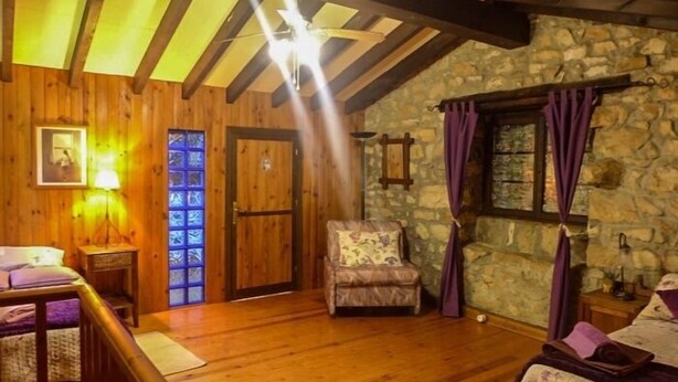A cozy room with wooden floors, a stone wall, a wooden door, a cushioned chair, and a small table with a lamp. - Casa Yolanda - country house in the Picos de Europa, Arenas de Cabrales (Arenas De Cabrales)