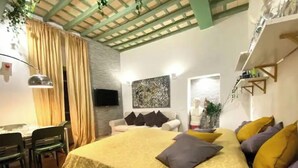 Une chambre à coucher avec un lit, un bureau et une chaise. Il y a un téléviseur accroché au mur et un tableau au-dessus du lit.