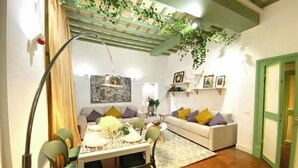 Un coin repas avec une table dressée pour quatre personnes, un canapé et une plante suspendue.