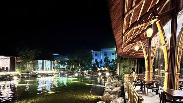 Vista nocturna de un restaurante con fuente de agua, paredes de piedra y barandillas de bambú.