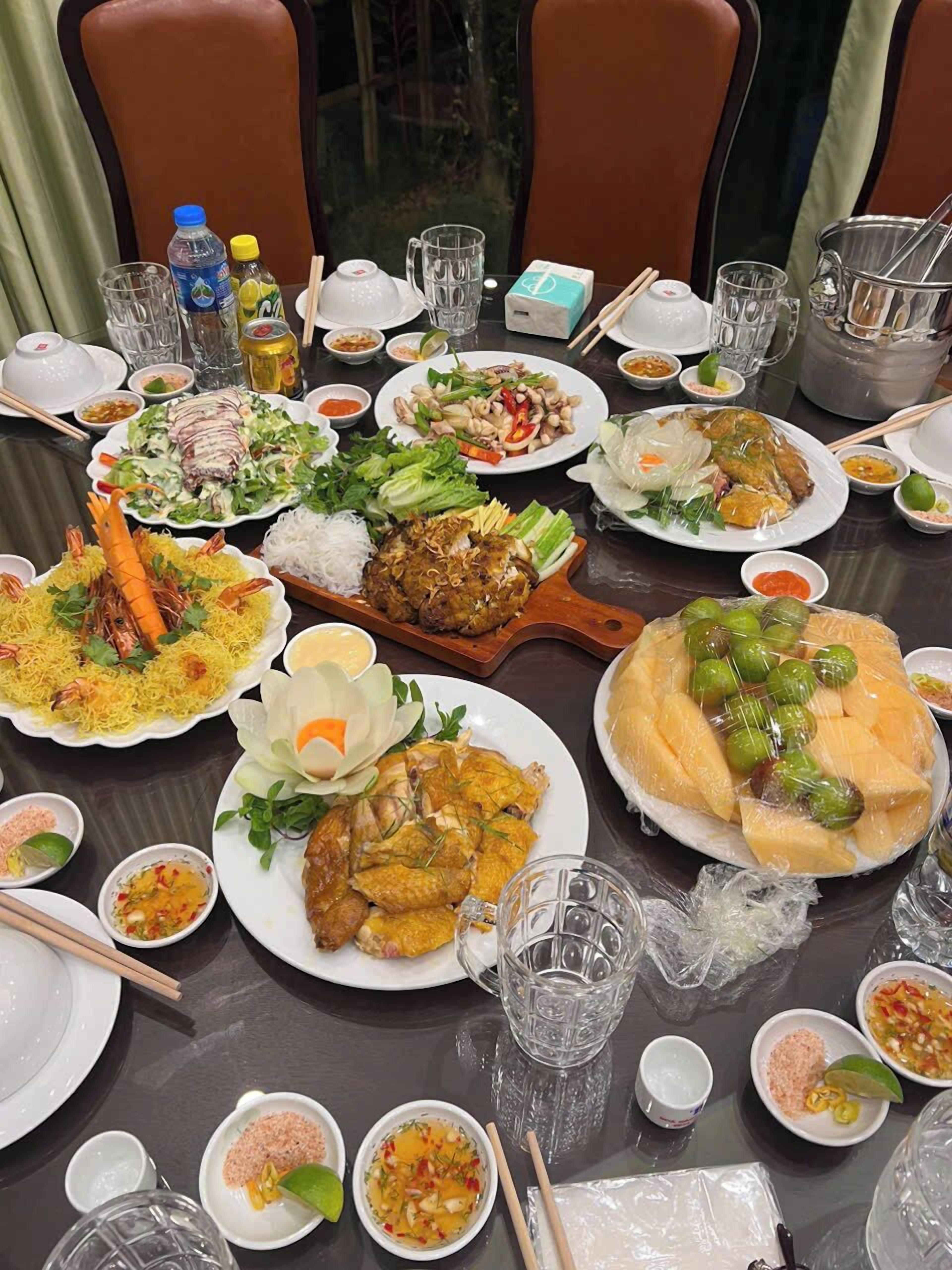 A dining table with various dishes, including seafood, vegetables, and rice, along with condiments and drinks.